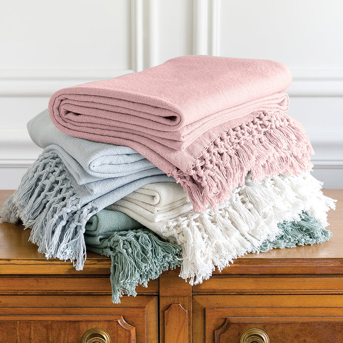 A stack of folded bed throws in various colors, including pink, white, and green, with fringed edges.